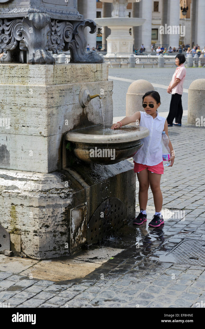 A young girl washing her hand in a water fountain in St Peter's Square, Vatican City, Rome, Italy. Stock Photo