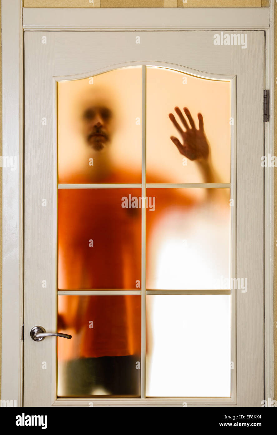 Silhouette of an unknown man in orange seen through a closed glass door, like a ghost or an alien Stock Photo