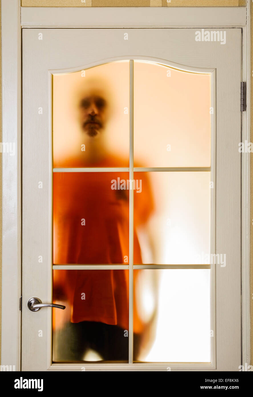 Silhouette of an unknown man in orange seen through a closed glass door, like a ghost or an alien Stock Photo