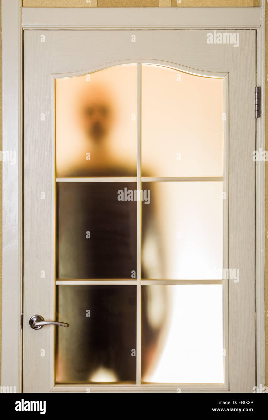 Silhouette of an unknown man in black seen through a closed glass door, like a ghost or an alien Stock Photo