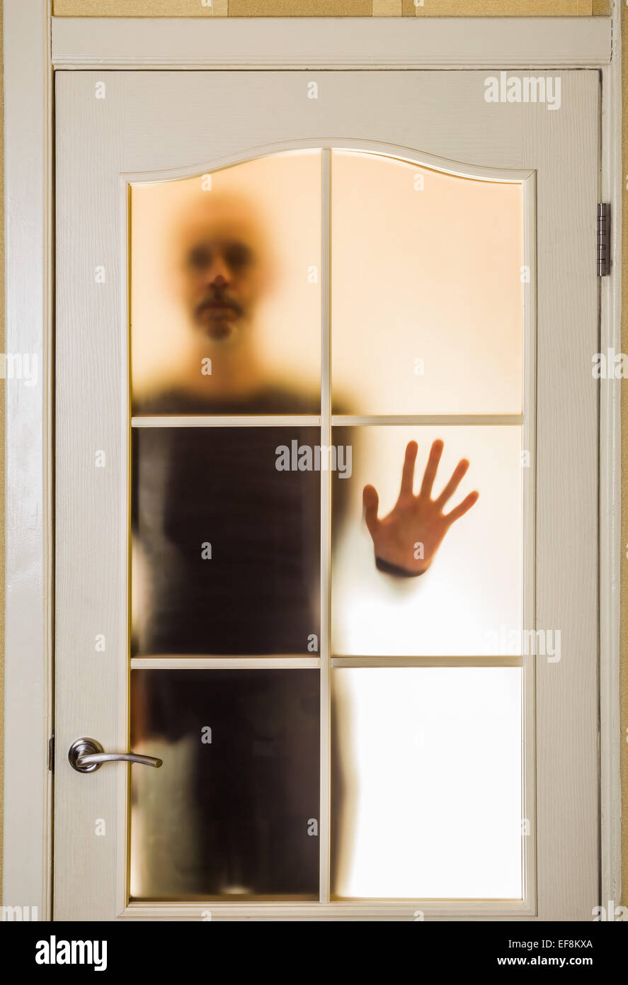 Silhouette of an unknown man in black  seen through a closed glass door, like a ghost or an alien Stock Photo