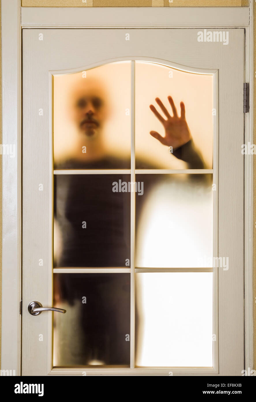 Silhouette of an unknown man in black  seen through a closed glass door, like a ghost or an alien Stock Photo