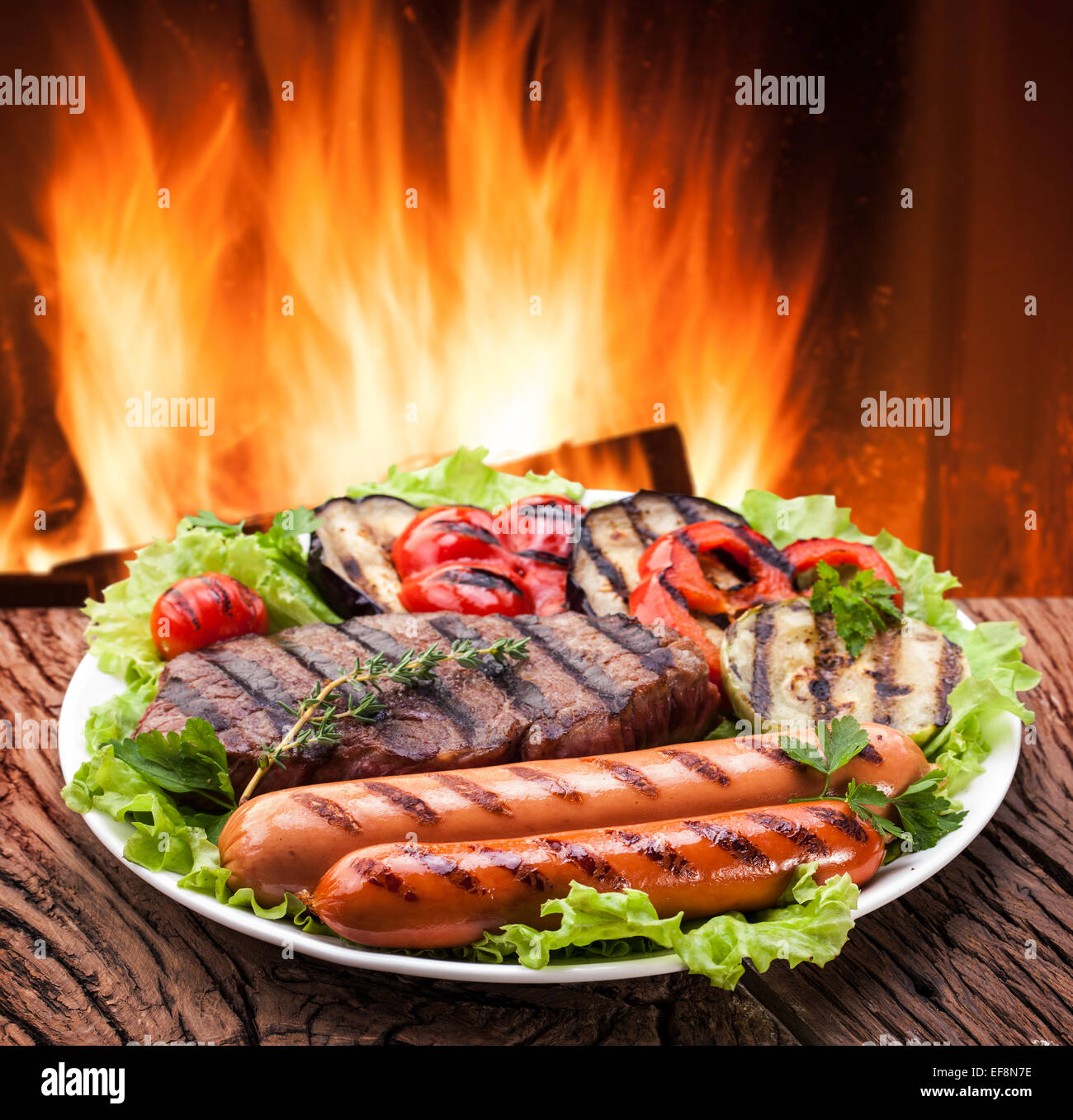 Grill: steak, sausage and vegetable on a plate. In the background - the fire. Stock Photo