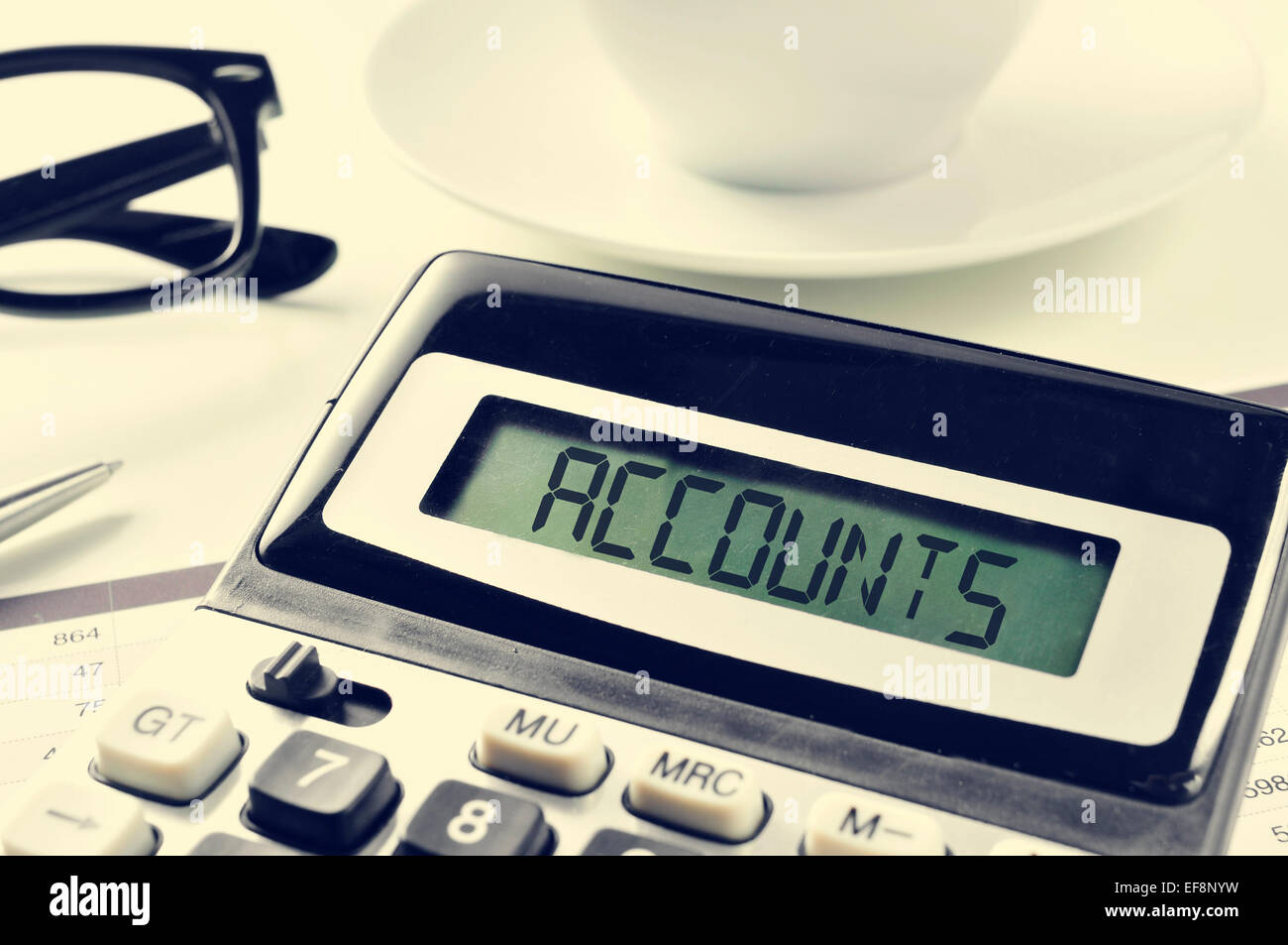the word accounts written in the display of a calculator on an office desk, with a cup of coffee or tea in the background Stock Photo