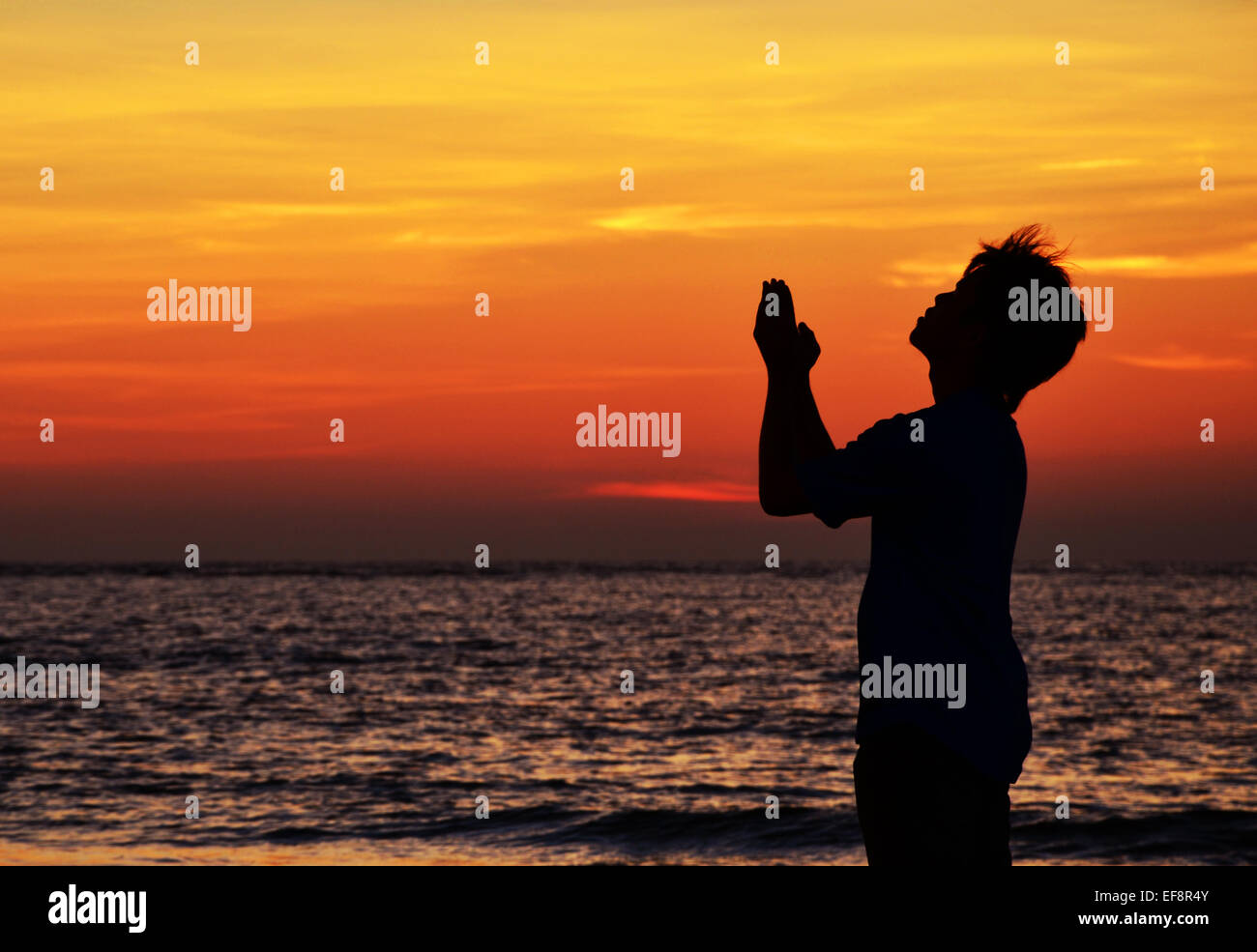 Malaysia, Sabah, Tuaran, Praying man silhouetted against sunset sky over sea Stock Photo
