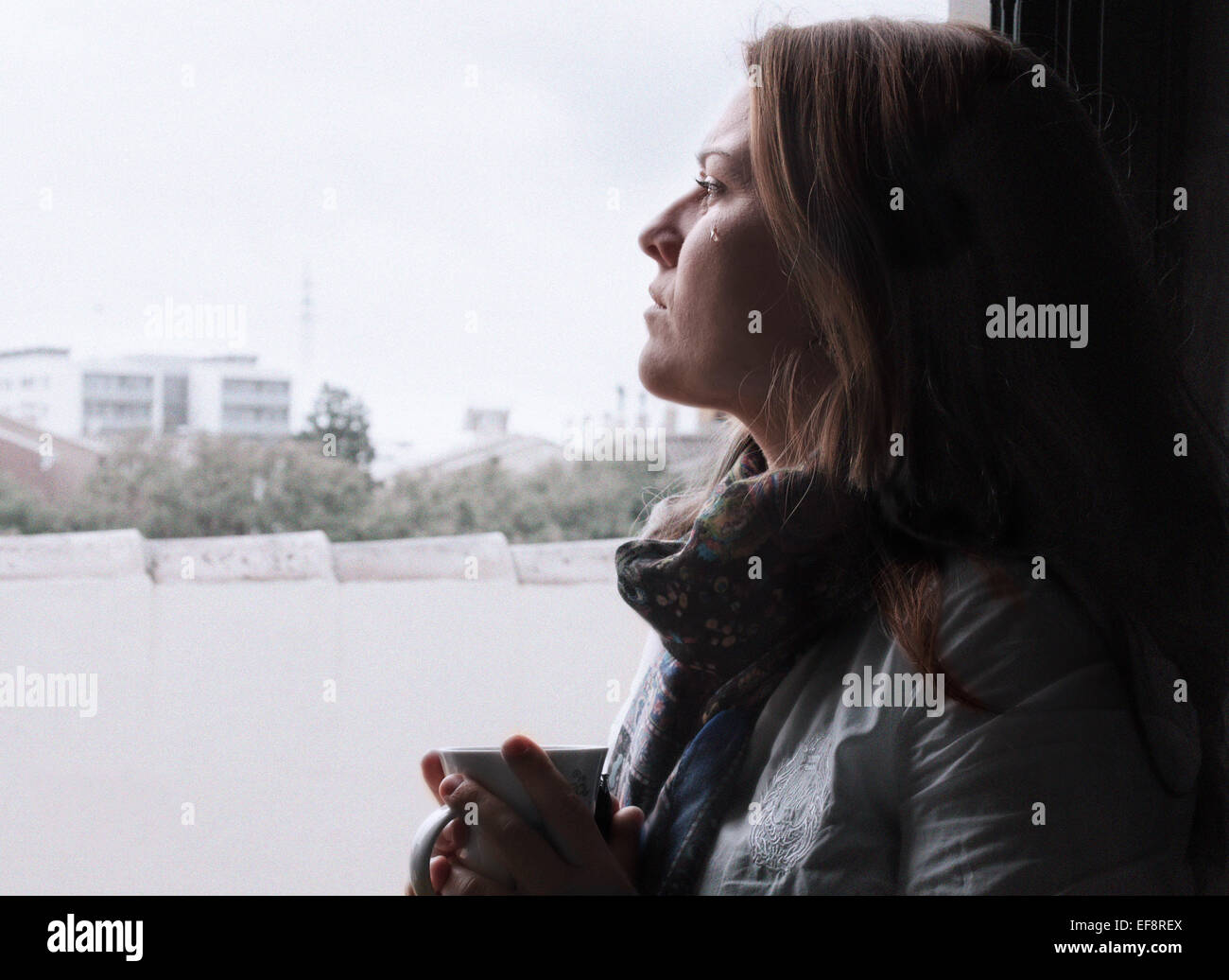 Crying woman looking through window Stock Photo