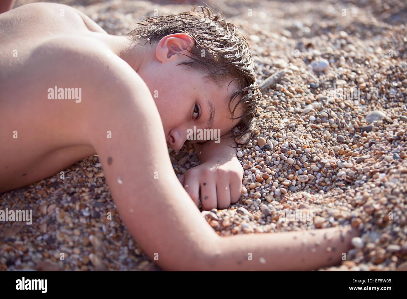 Young boy (12-13) laying on sandy beach Stock Photo