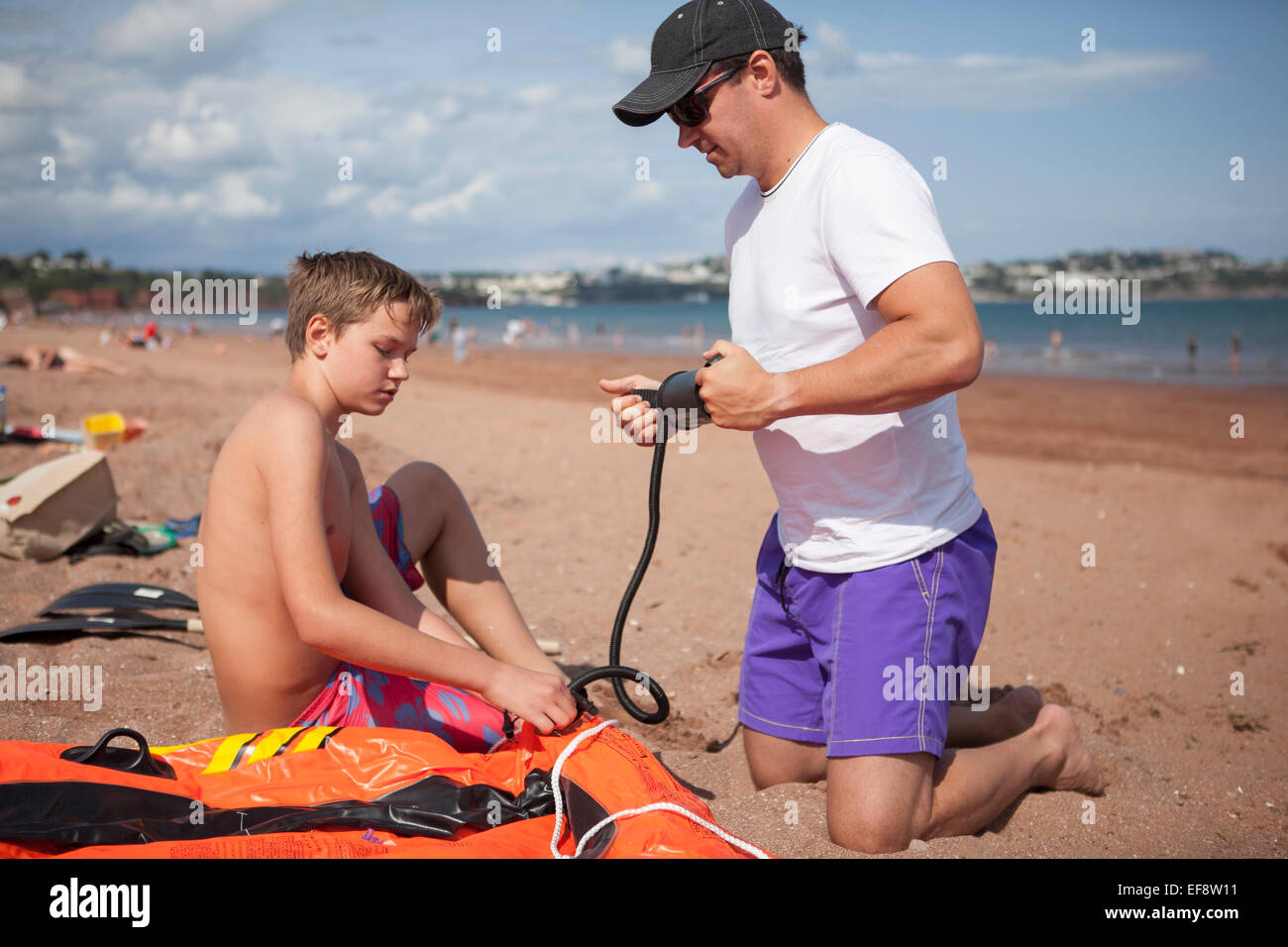 Father and son (12-13) inflating boat on beach Stock Photo