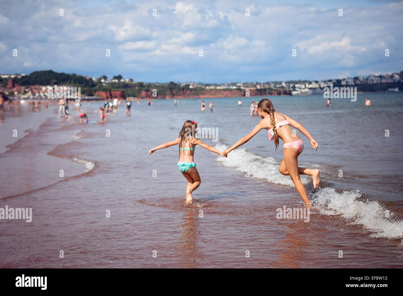 Two girl (4-5, 12-13) running along beach Stock Photo