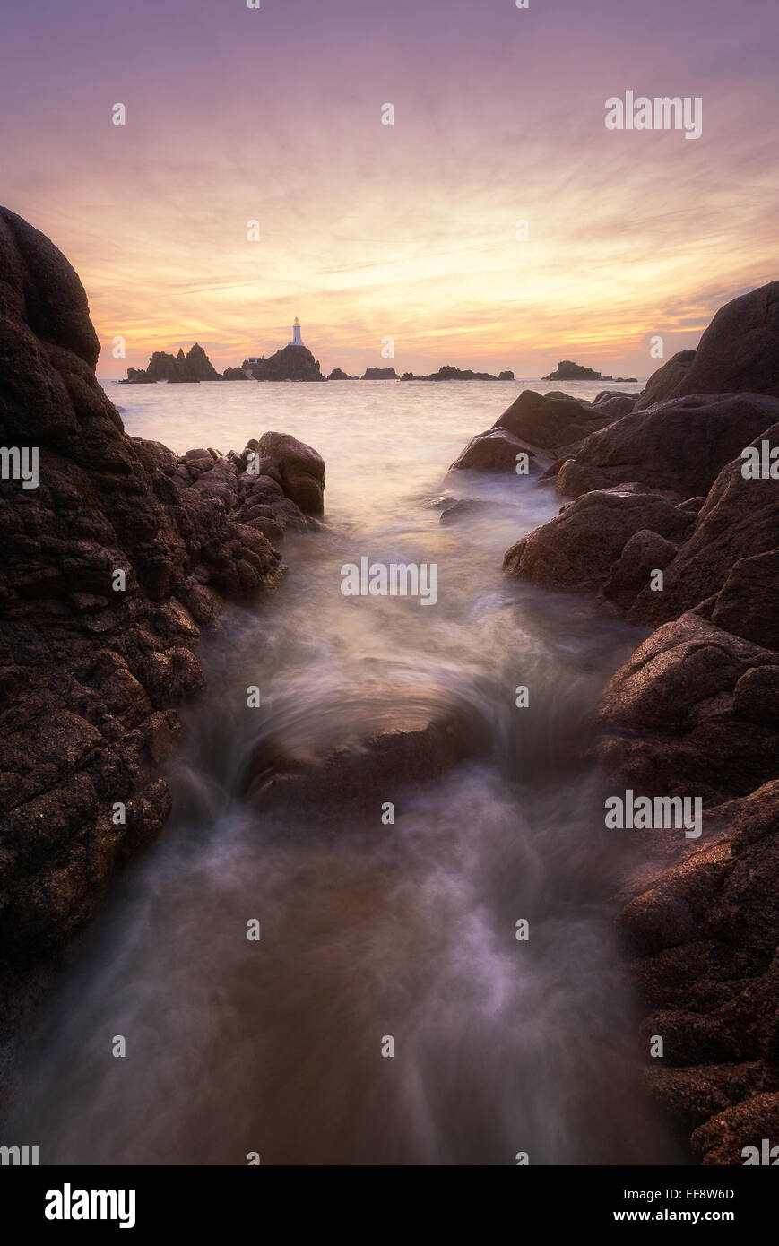 Jersey, La Corbiere, Seawater flowing in-between rocks with lighthouse seen at horizon Stock Photo