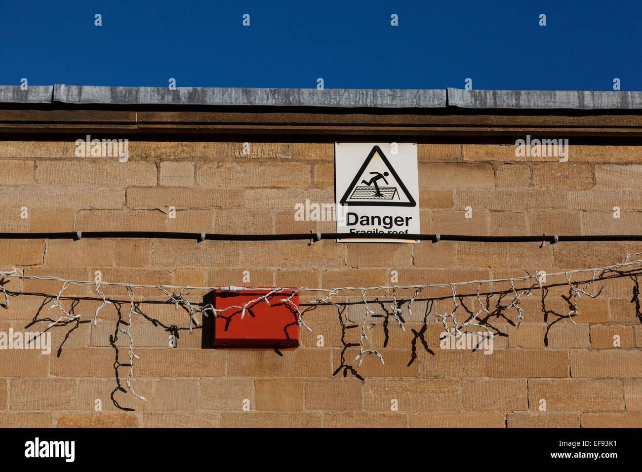 Danger 'fragile roof' sign on a stone wall with Christmas Lights