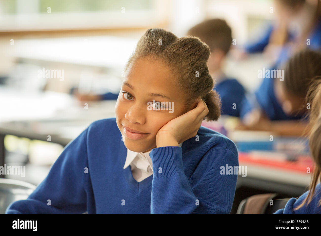 Portrait of smiling elementary school girl sitting bored in classroom Stock Photo