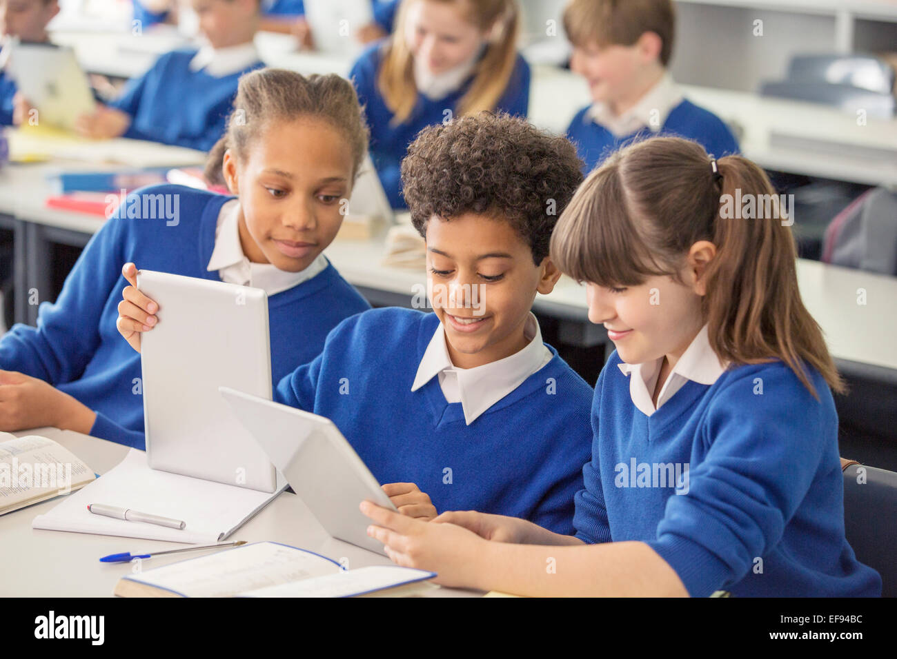 Elementary school children wearing blue school uniforms using digital tablets at desk in classroom Stock Photo