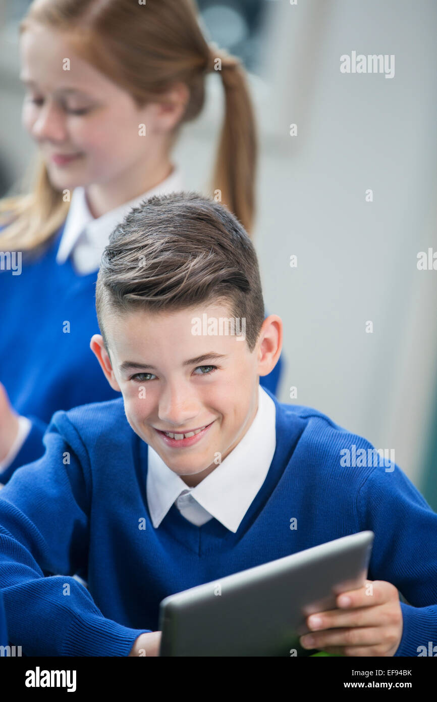 Portrait of cheerful schoolboy wearing blue school uniform with tablet pc in classroom Stock Photo