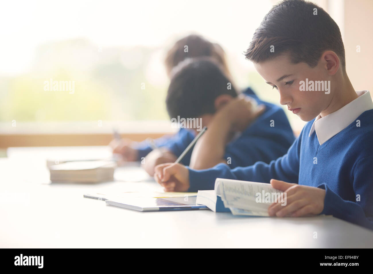 Pupil learning in classroom using book and tablet pc Stock Photo