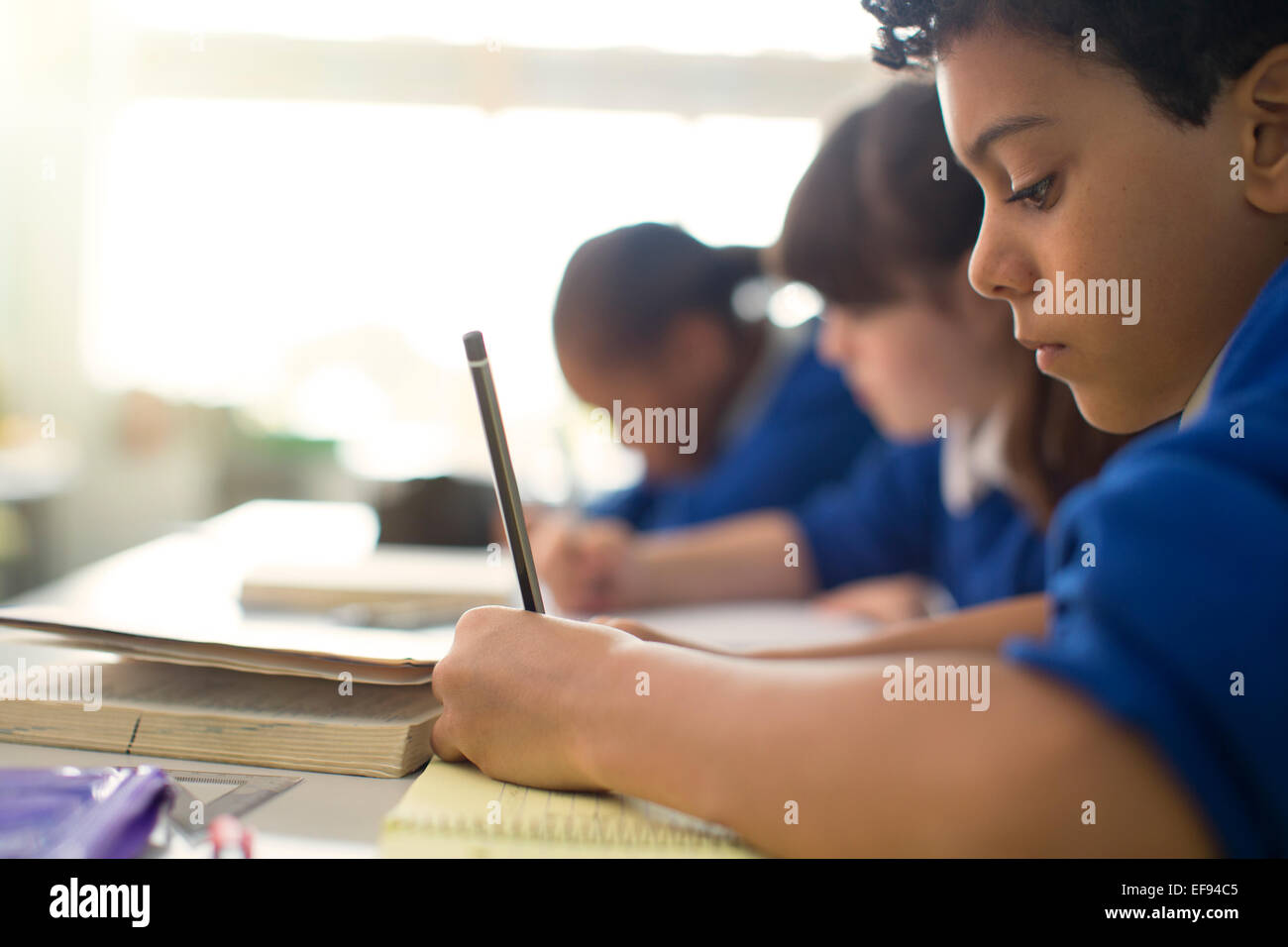 Pupils writing in notebooks at desks in classroom Stock Photo
