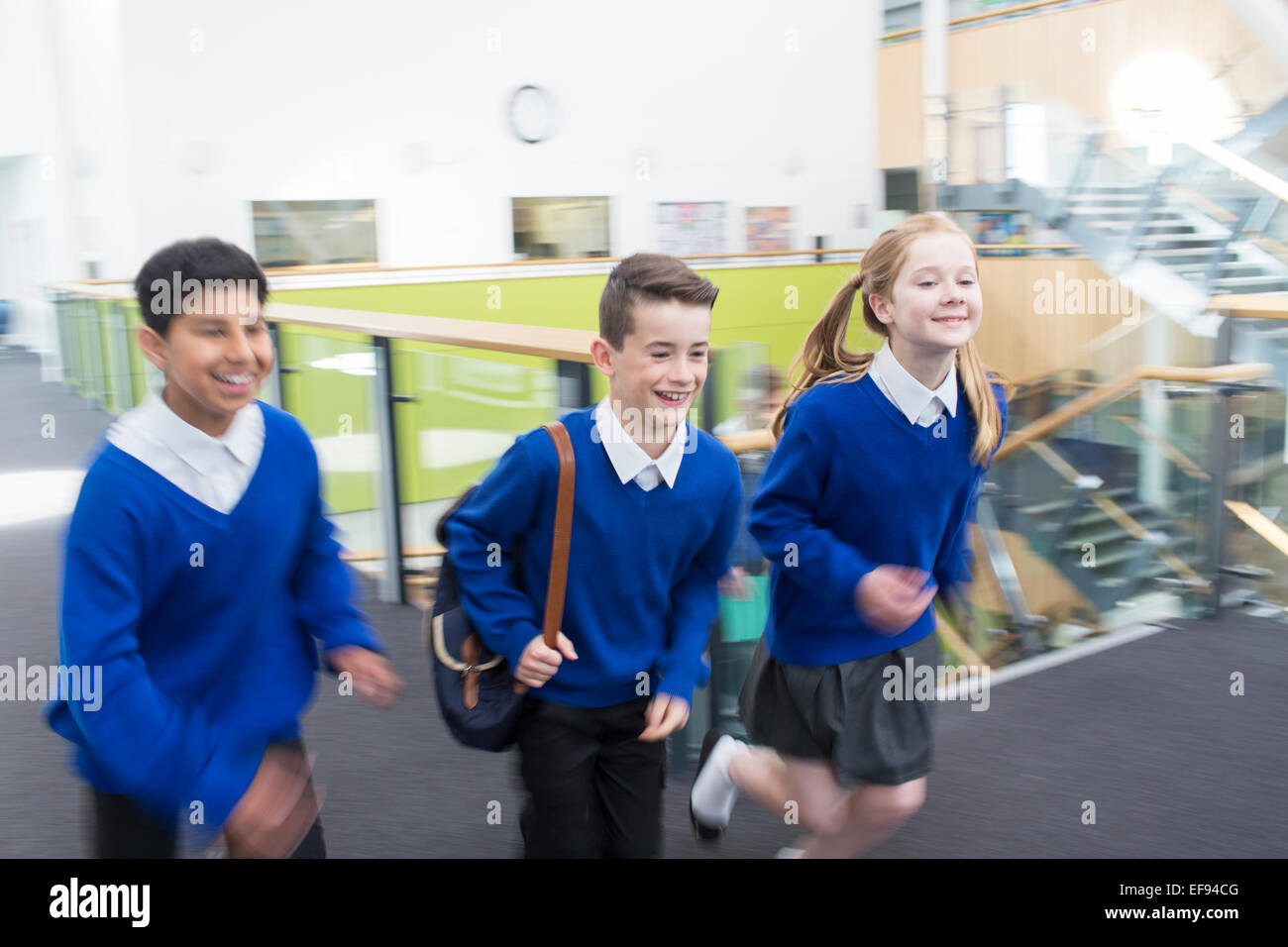 Happy pupils wearing school uniforms running in school corridor Stock Photo
