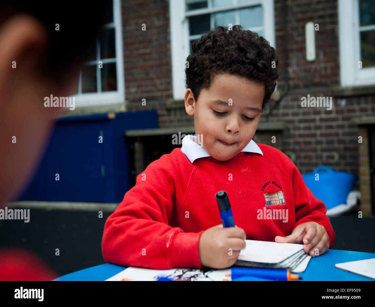 Afro-Caribbean boy playing and drawing outdoors in the playground of  Primary school in London W2 Stock Photo