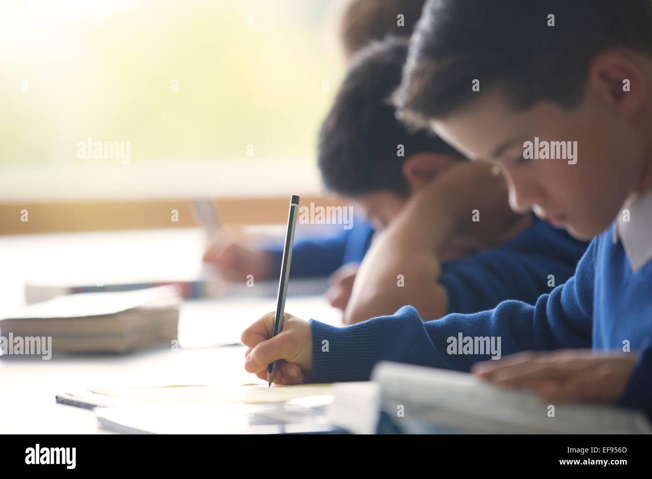 Schoolboys writing in notebook at desk in classroom Stock Photo