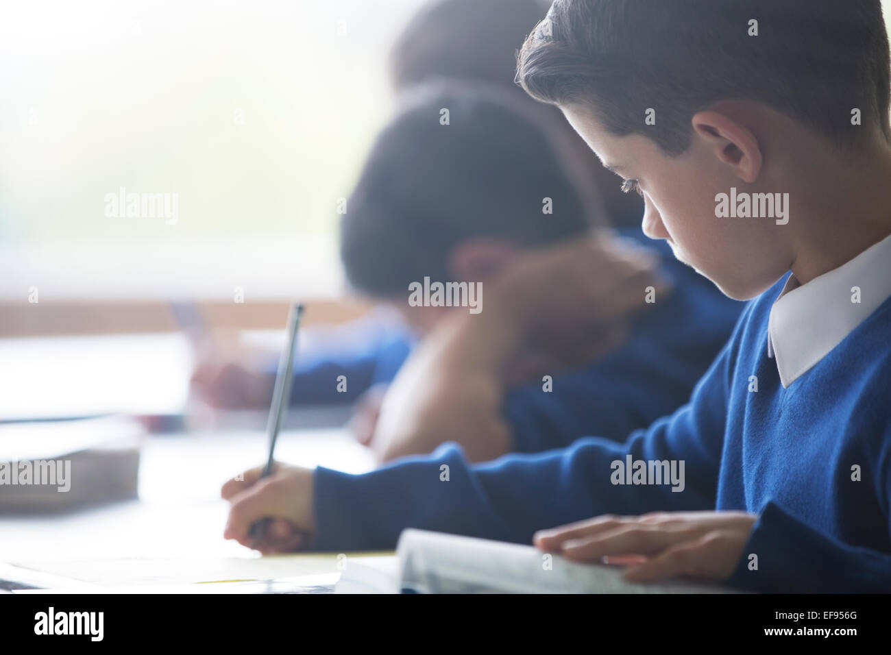 Schoolboys writing at desk in classroom Stock Photo