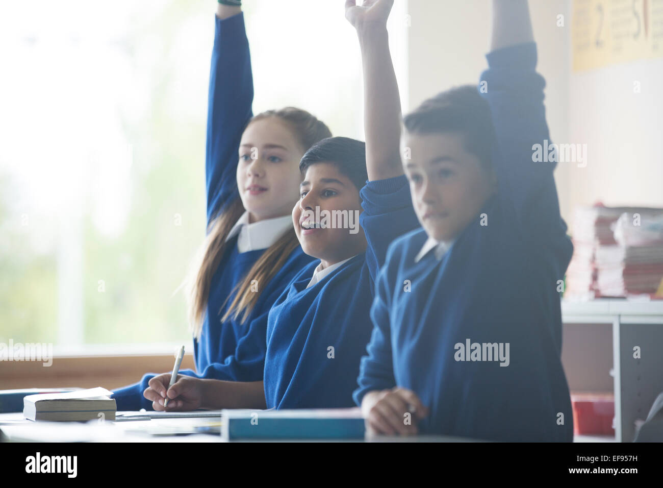 Primary school children in classroom raising arms Stock Photo