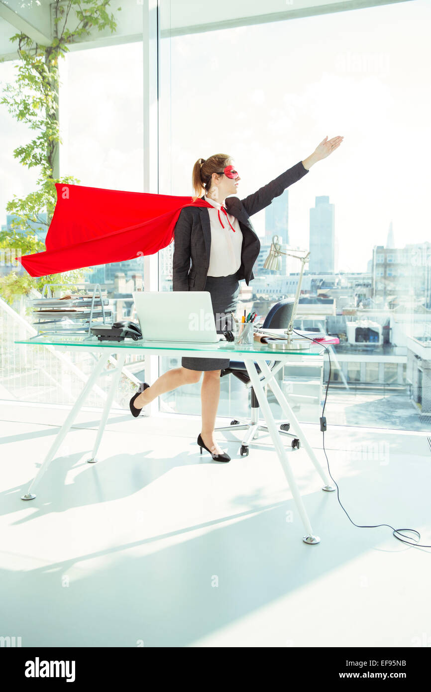Businesswoman preparing to fly in cape and mask in office Stock Photo