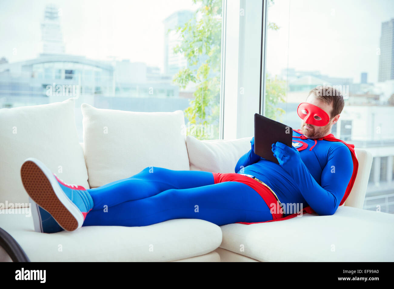Superhero using digital tablet on living room sofa Stock Photo