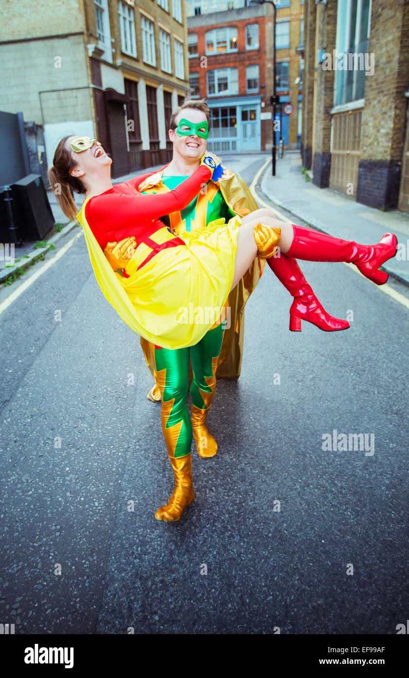 Superhero carrying wife on city street Stock Photo