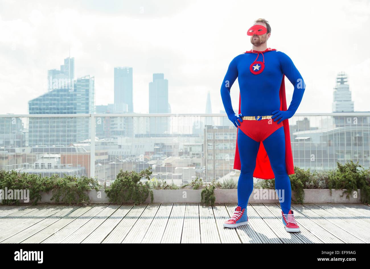 Superhero standing with hands on hips on city rooftop Stock Photo