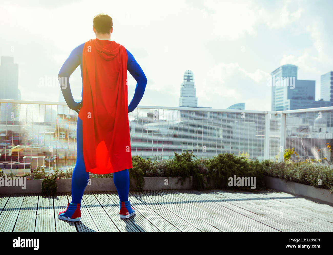Superhero looking at view from city rooftop Stock Photo