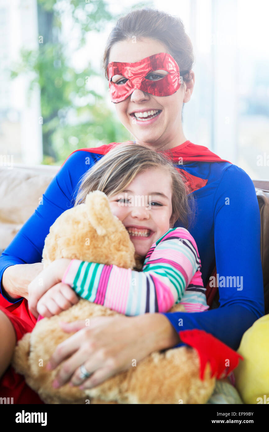 Superhero mother hugging daughter on sofa Stock Photo