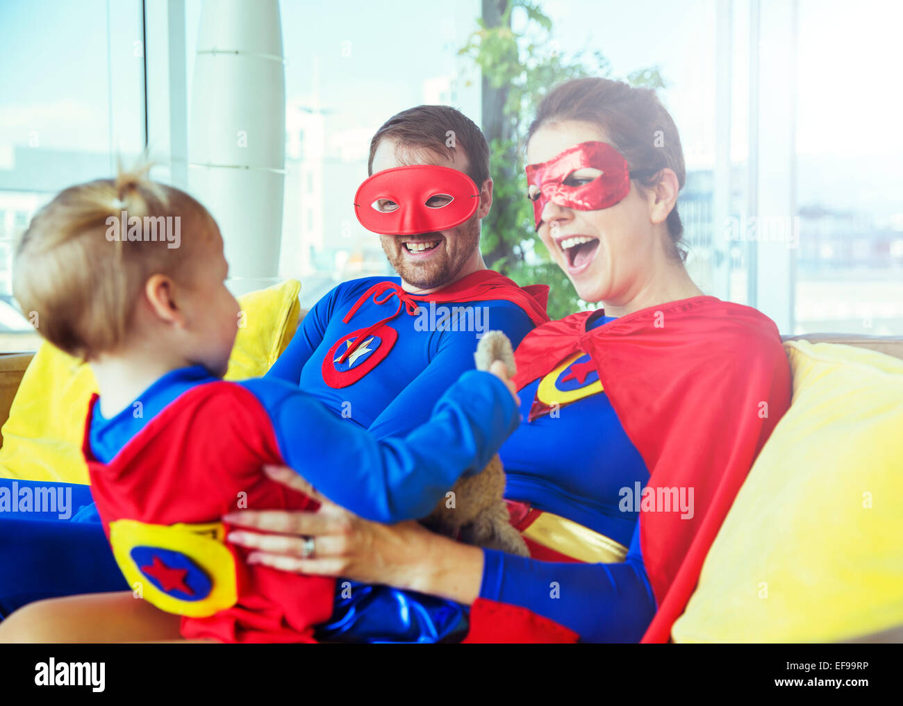 Superhero parents playing with daughter on living room sofa Stock Photo