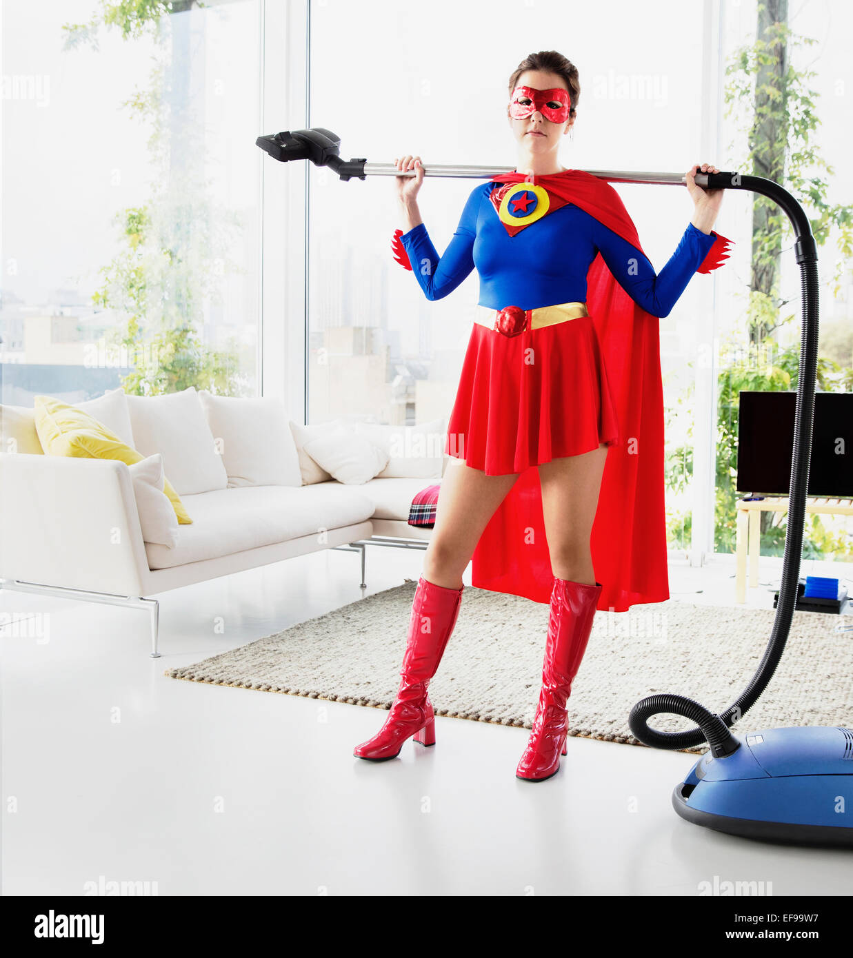 Superhero holding vacuum in living room Stock Photo