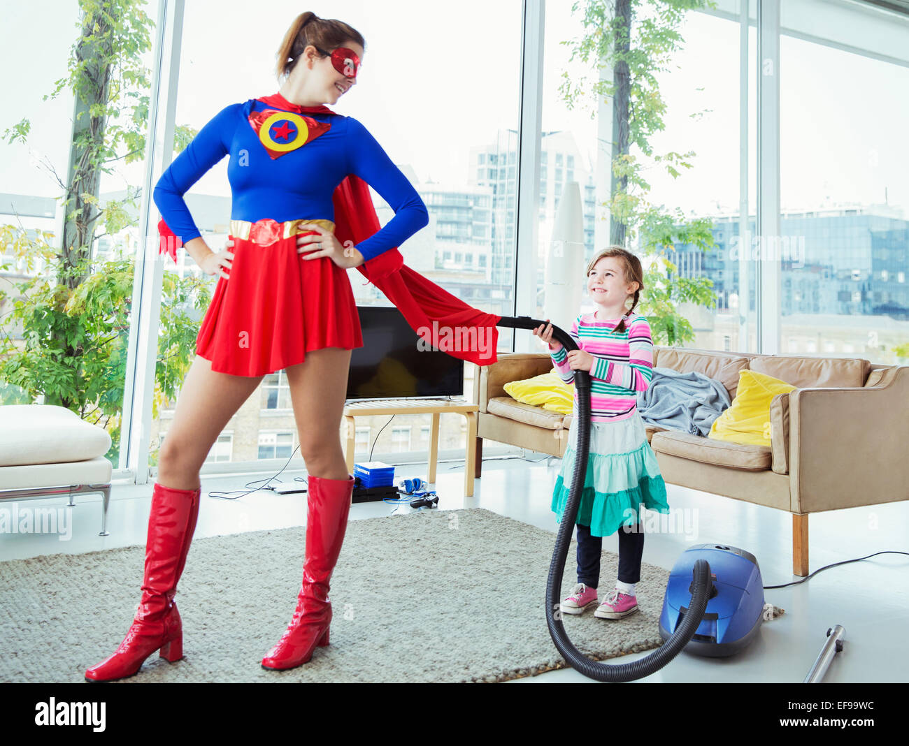 Daughter of superhero vacuuming her cape in living room Stock Photo