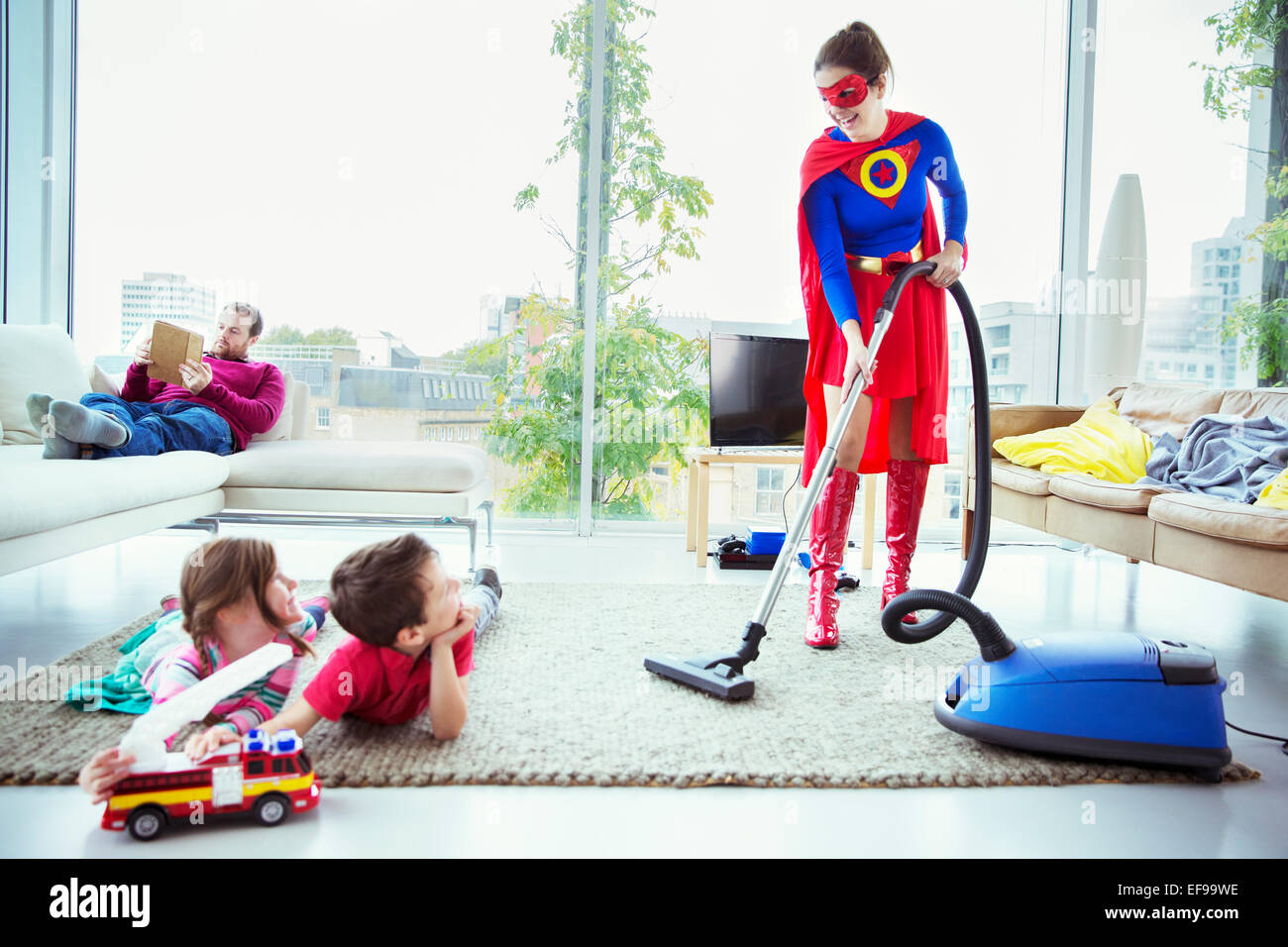 Superhero vacuuming around family in living room Stock Photo