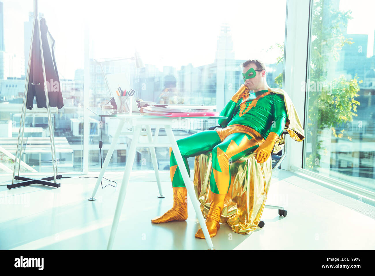 Bored superhero slouching at desk in office Stock Photo