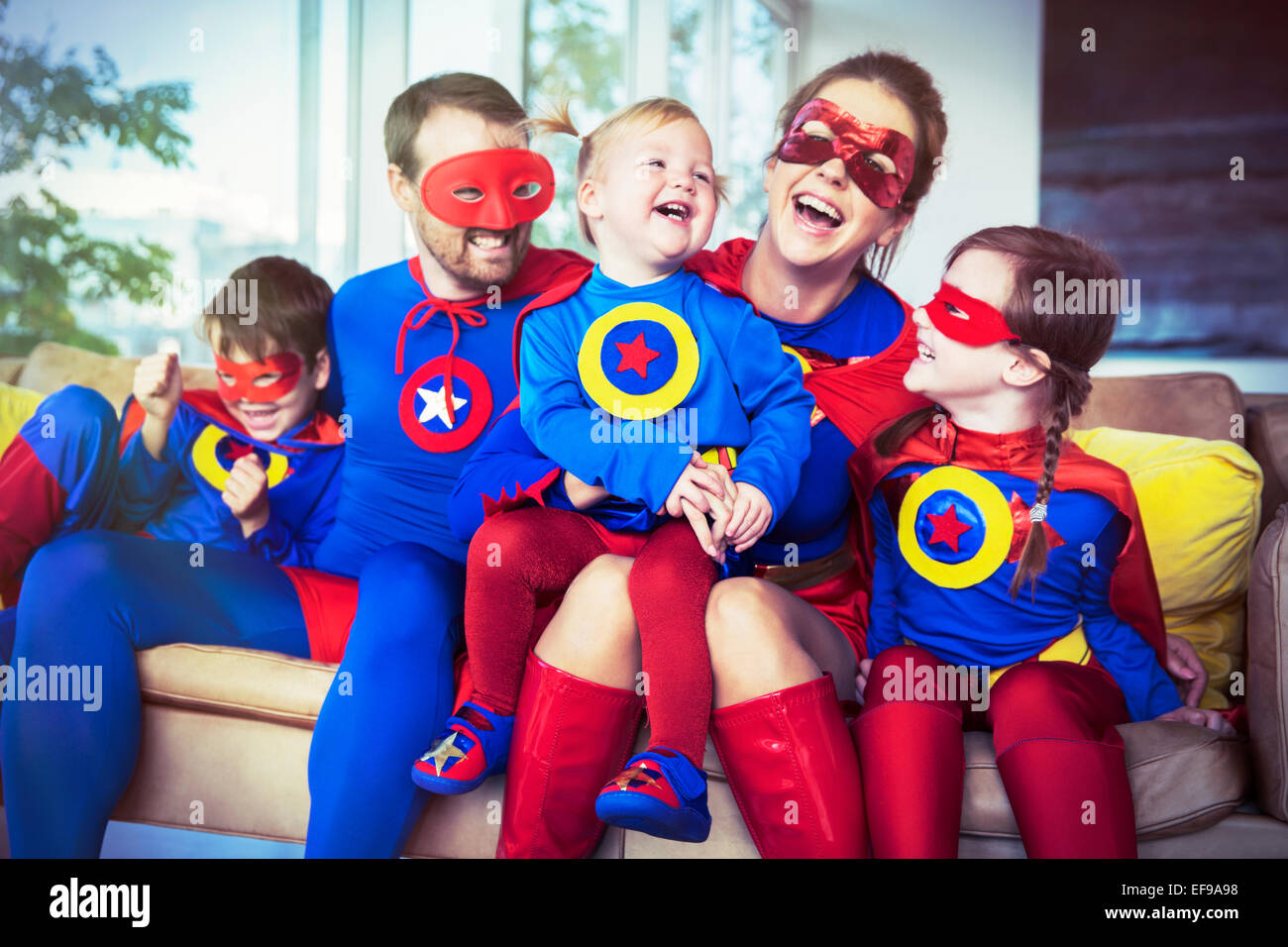 Superhero family laughing on sofa Stock Photo