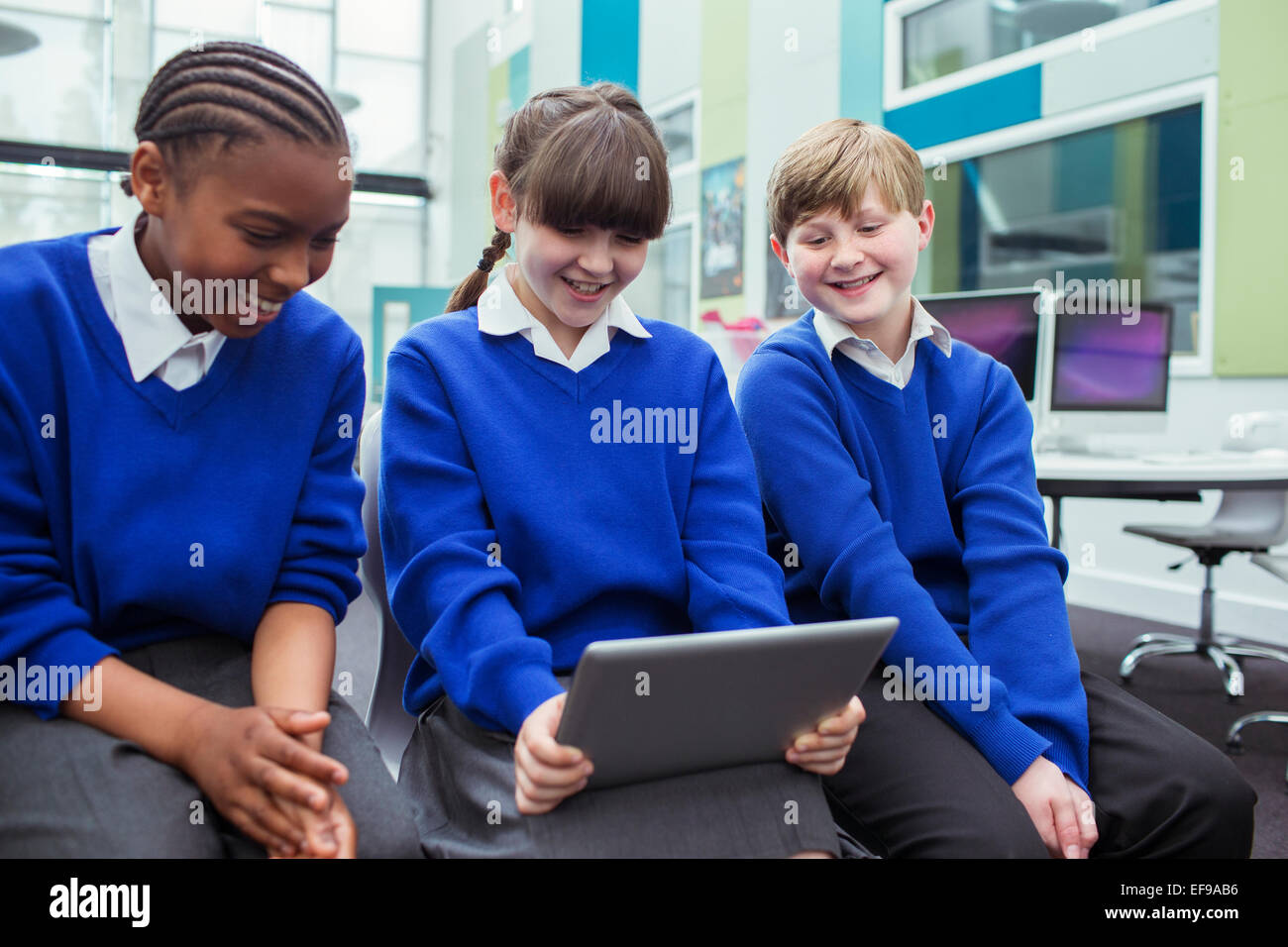 Primary school children wearing blue school uniforms holding digital tablet and smiling in classroom Stock Photo