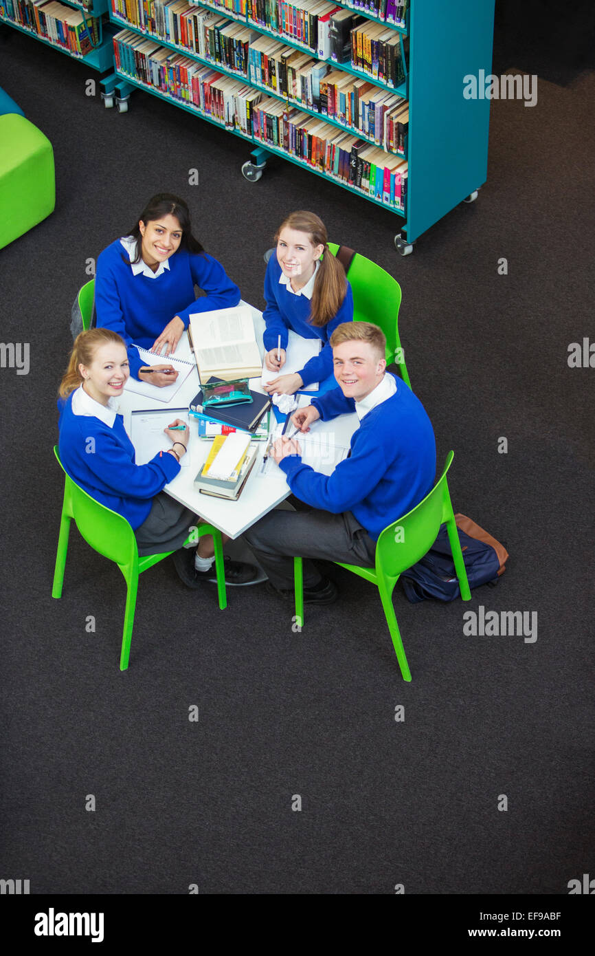Overhead view of four students doing their homework at round table, looking at camera Stock Photo