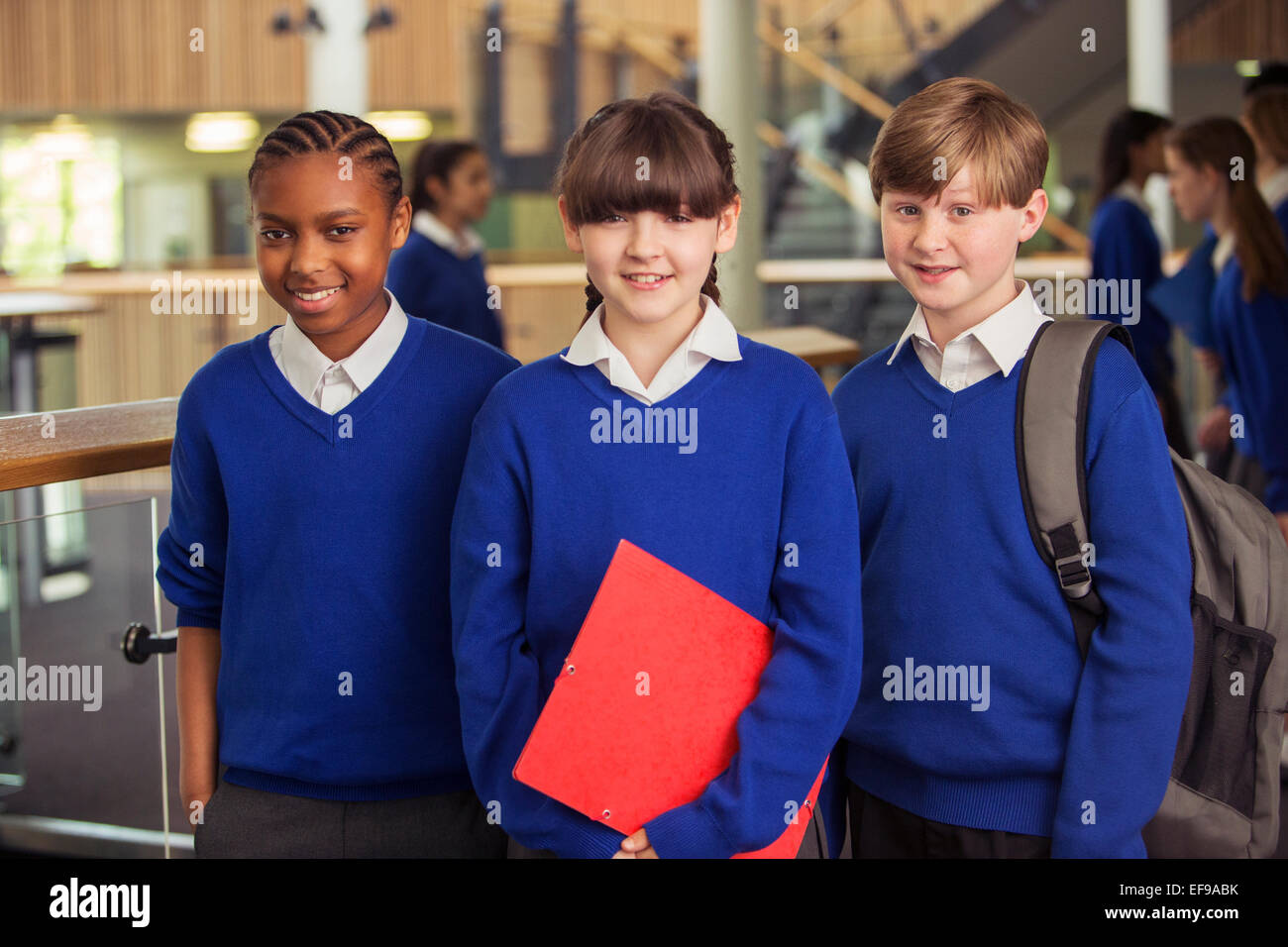 Portrait of three elementary school children wearing blue school uniforms standing in corridor Stock Photo