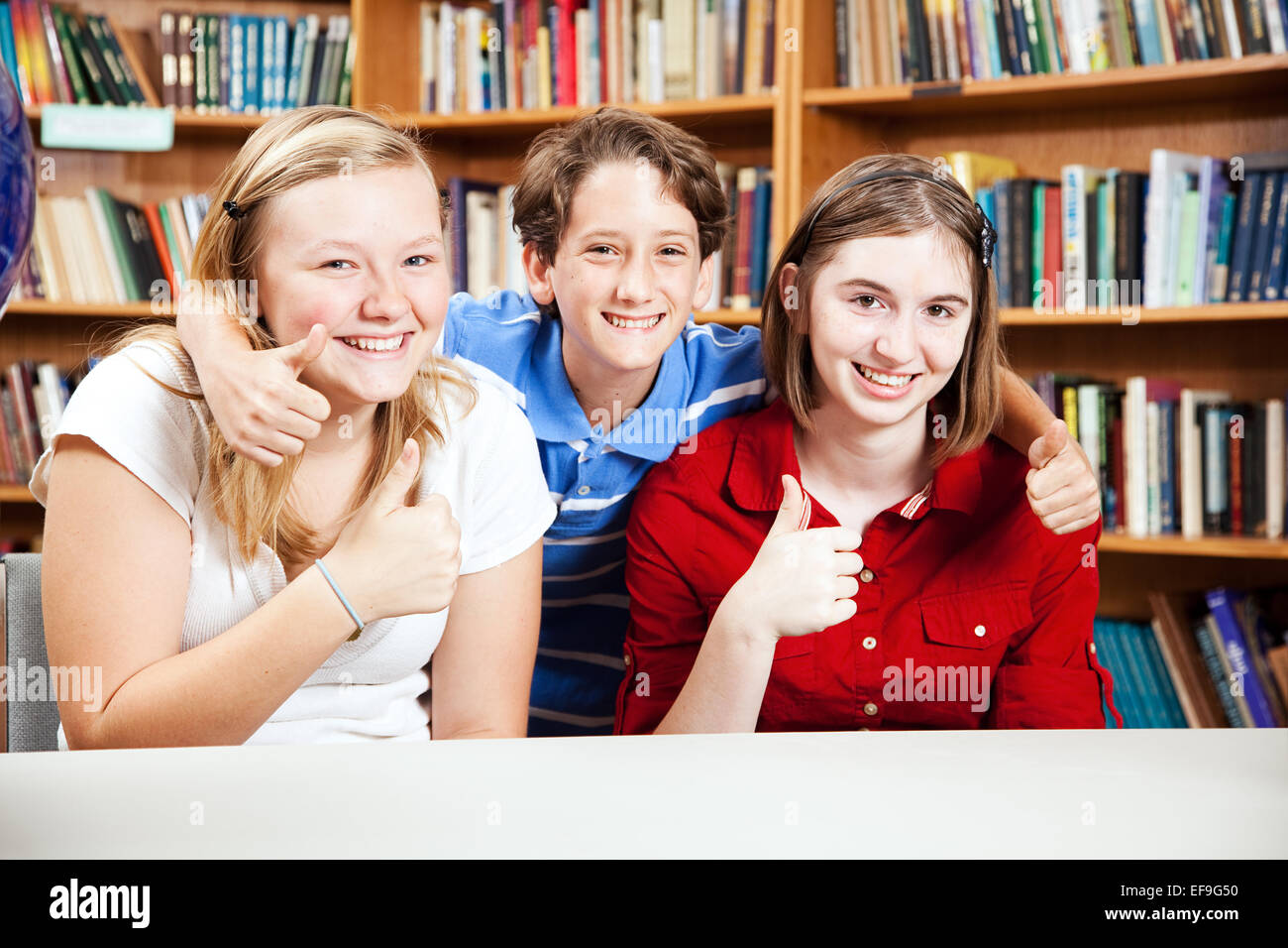 Three school kids giving thumbs up in the library Stock Photo - Alamy
