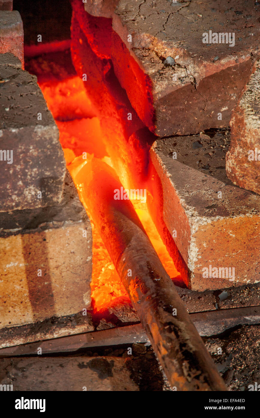 An iron bar is heated red-hot in the forge of a blacksmith's shop. Note fire bricks. Stock Photo
