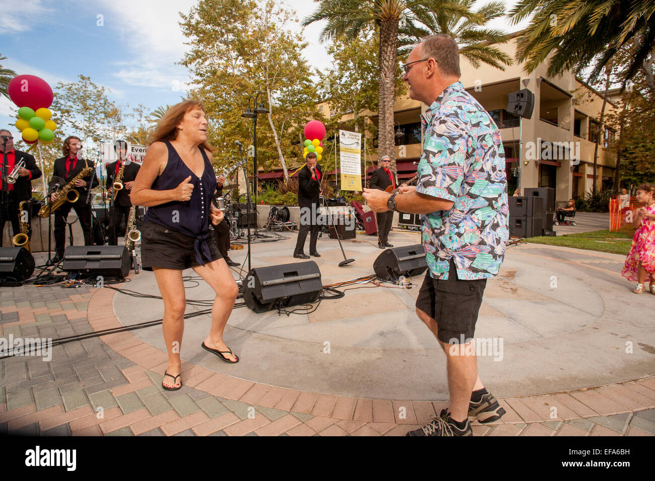 A middle aged couple dance to live band music at an outdoor concert in