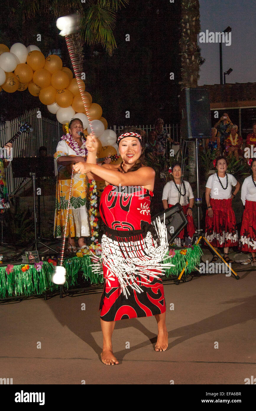 At a Hawaiian festival in Laguna Woods, CA, a costumed performer swings poi weights through a variety of rhythmical and geometric patterns. Poi originated with the Māori people of New Zealand. Note Hawaiian musicians in background. Stock Photo