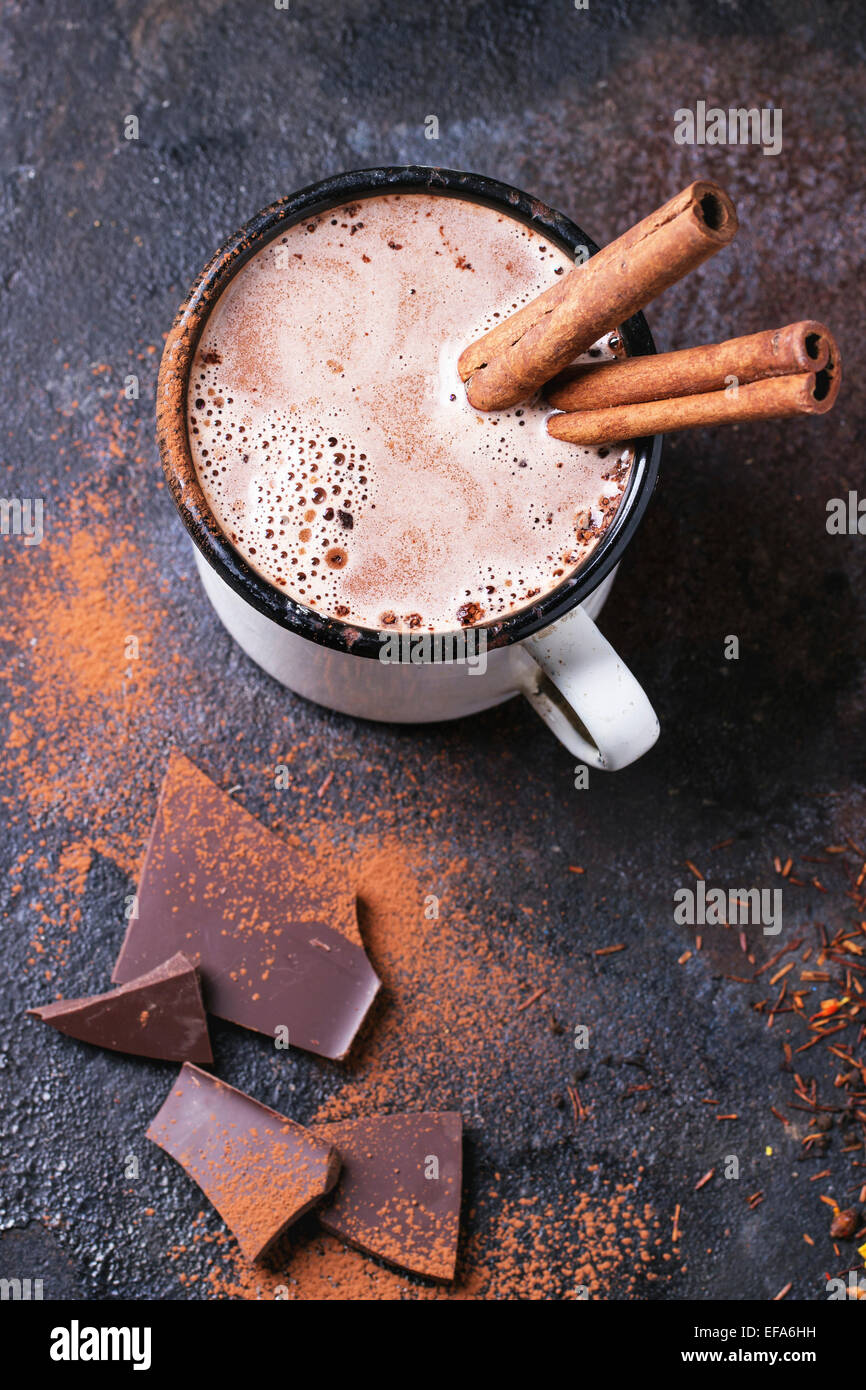 Vintage mug of hot chocolate with cinnamon sticks over dark background Stock Photo