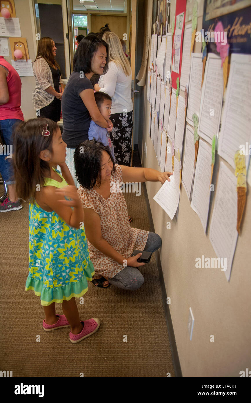 Asian American students and mothers read student essays displayed on an Irvine, CA, elementary school classroom wall on parents day. Stock Photo