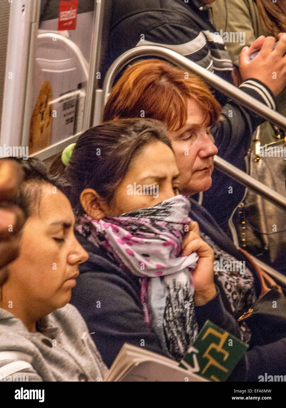 A woman with a cold covers her mouth with a scarf while traveling in a subway car in New York City. Stock Photo