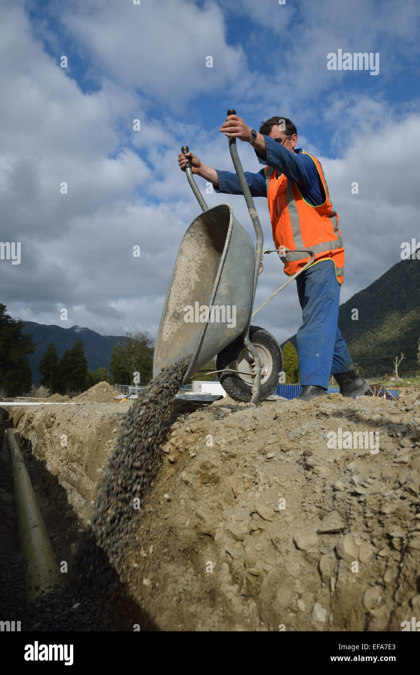 A tradesman tips gravel into a new stormwater drain Stock Photo