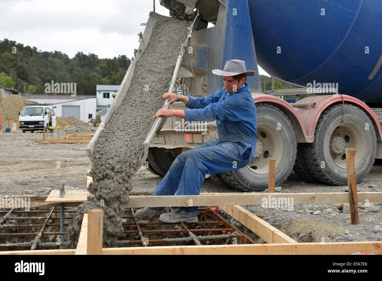 A builder directs wet concrete from a cement truck into the foundations of a large building. Stock Photo