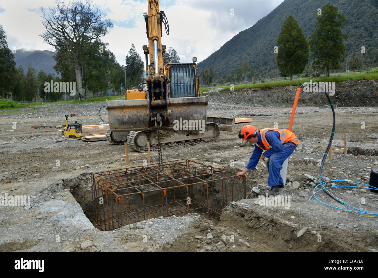 A builder directs a cage of reinforcing rods into the foundation for a portal a large building Stock Photo
